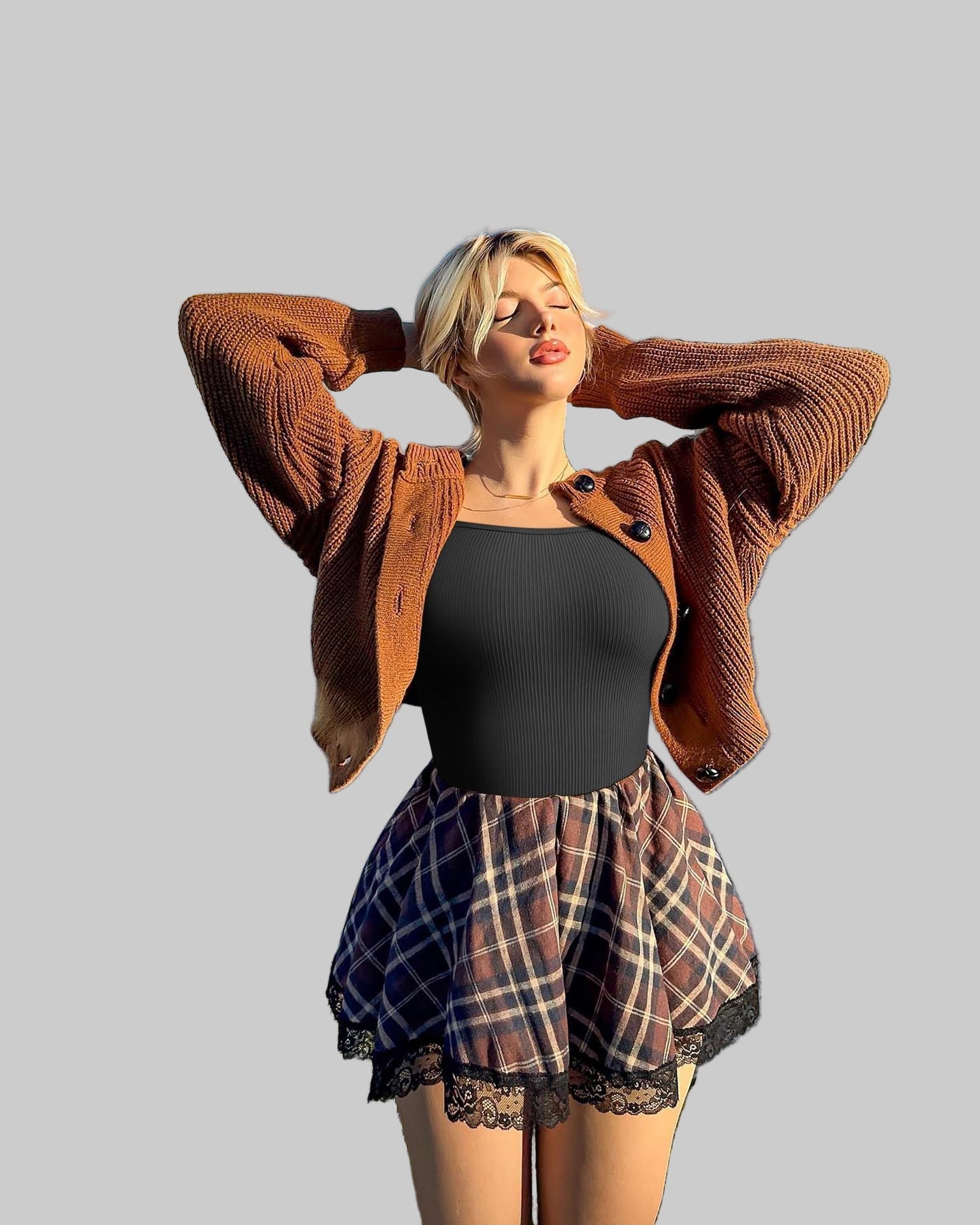 Woman wearing a brown cardigan, black top, and plaid skirt outdoors with a palm tree in the background.