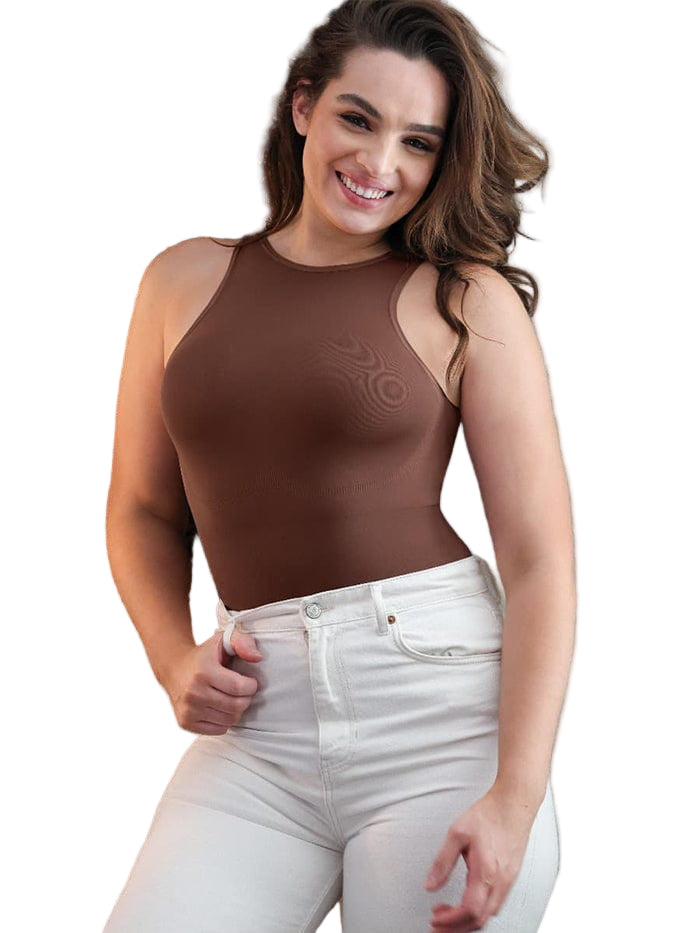 Woman wearing a brown sleeveless top and white pants with a decorative wall in the background.