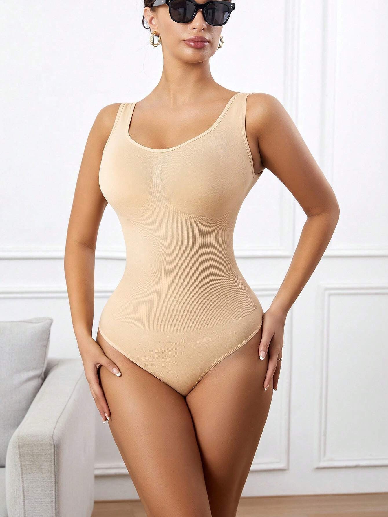 Woman wearing a beige bodysuit in a room with a neutral background