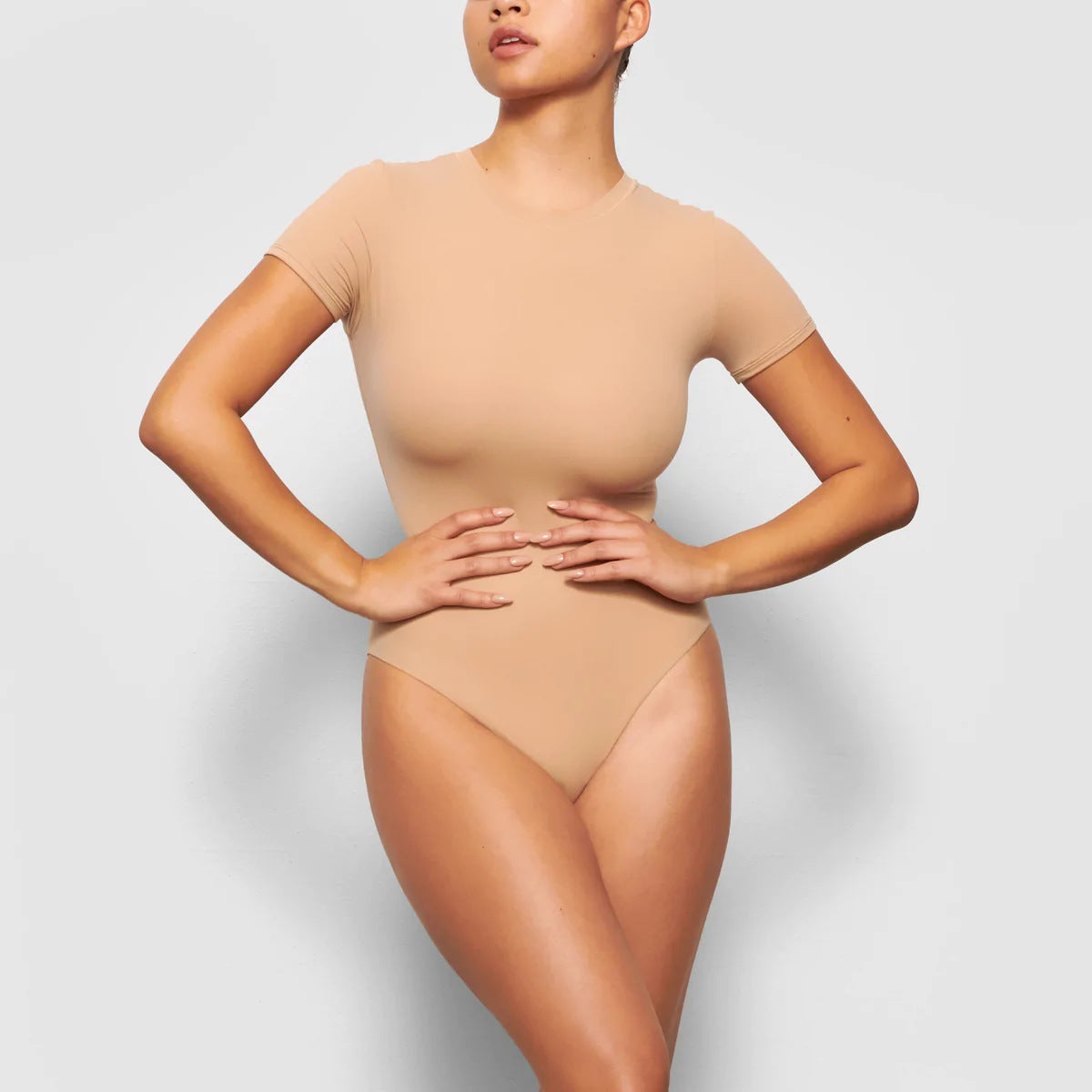 Beige bodysuit worn by a model on a light gray background