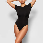 Person wearing a black bodysuit against a light gray background