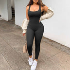 Person wearing a black jumpsuit with white sneakers on a sidewalk.