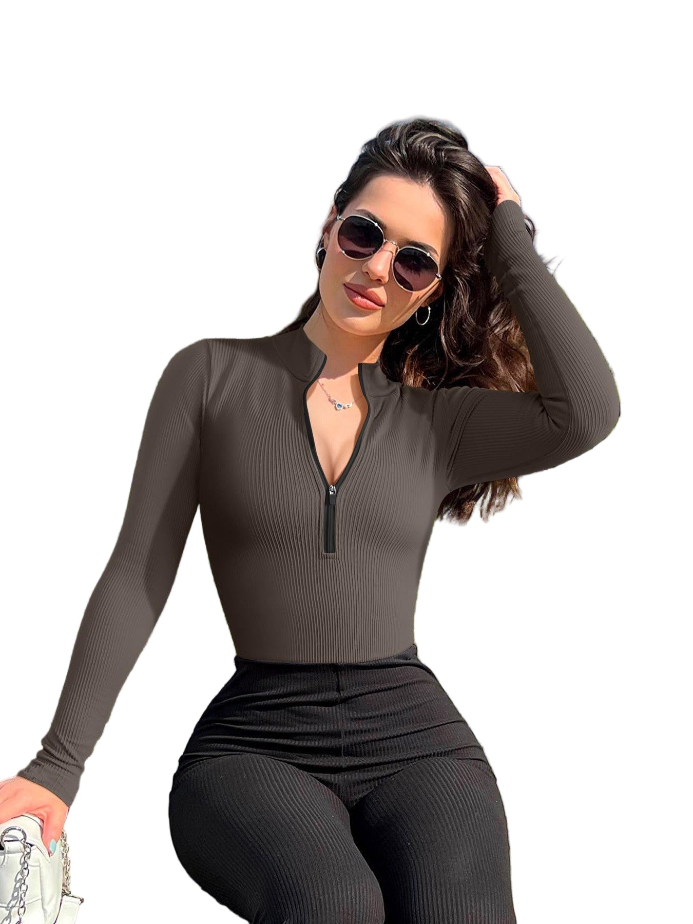 Woman in a brown long-sleeve top and black pants sitting outdoors with greenery and flags in the background.