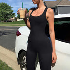 Person in a black bodysuit holding a drink, standing next to a white car on a residential street.