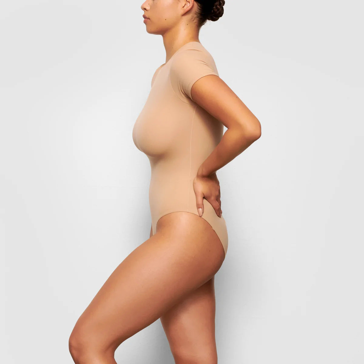 Person wearing a beige bodysuit against a light gray background