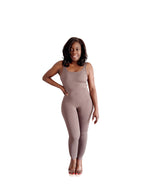 Woman wearing a beige jumpsuit standing in a room with light-colored walls and wooden flooring.