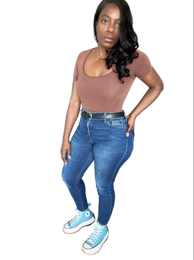 Woman wearing a brown top and blue jeans with blue sneakers in a kitchen.