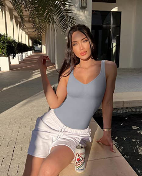 Woman in a blue swimsuit and white shorts sitting by a poolside.