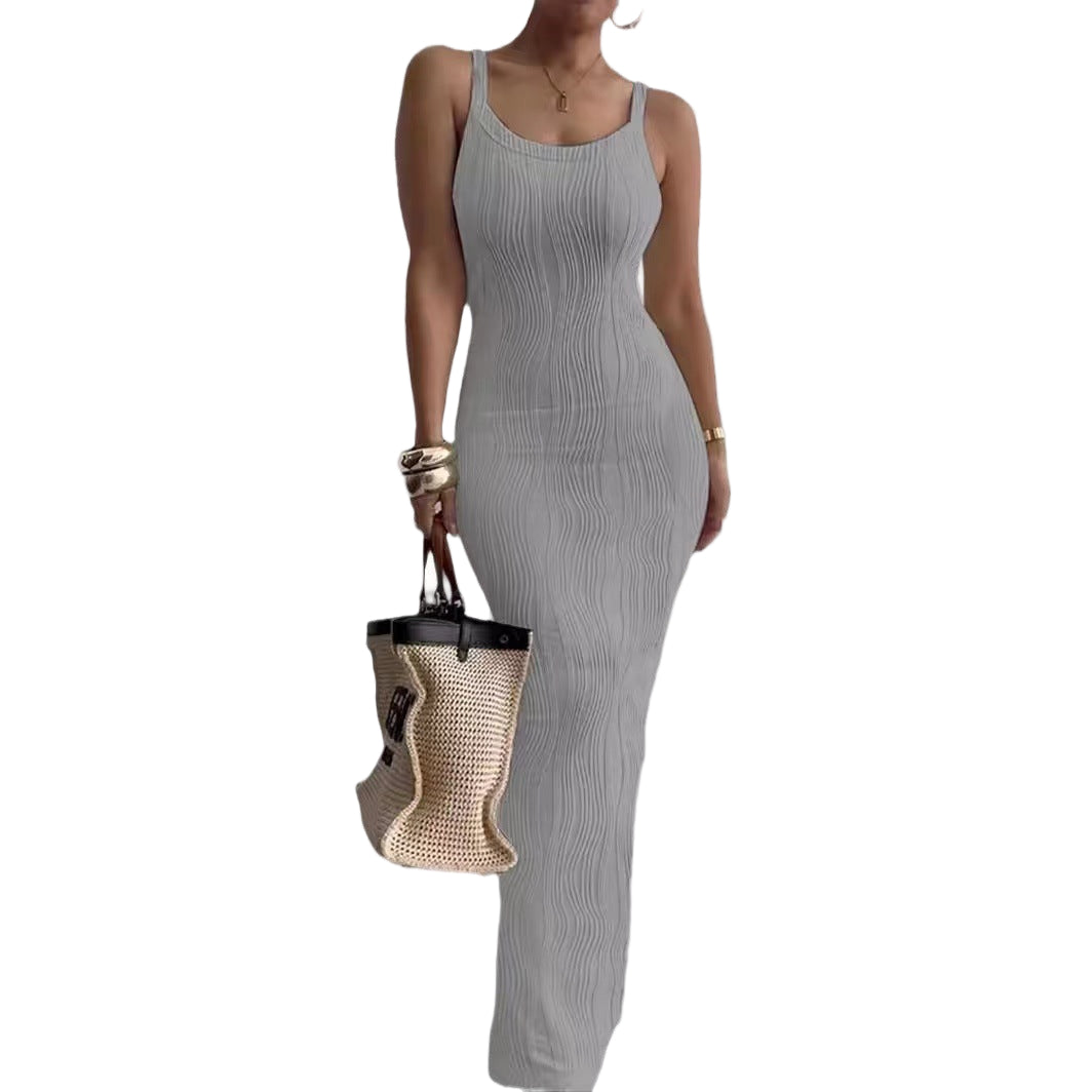 Woman wearing a gray ribbed jumpsuit holding a woven bag on a white background